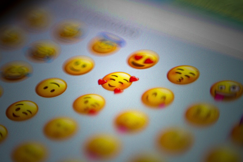 Tela de celular com vários emojis amarelos, um deles no centro com olhos fechados e três corações vermelhos ao redor, indicando amor